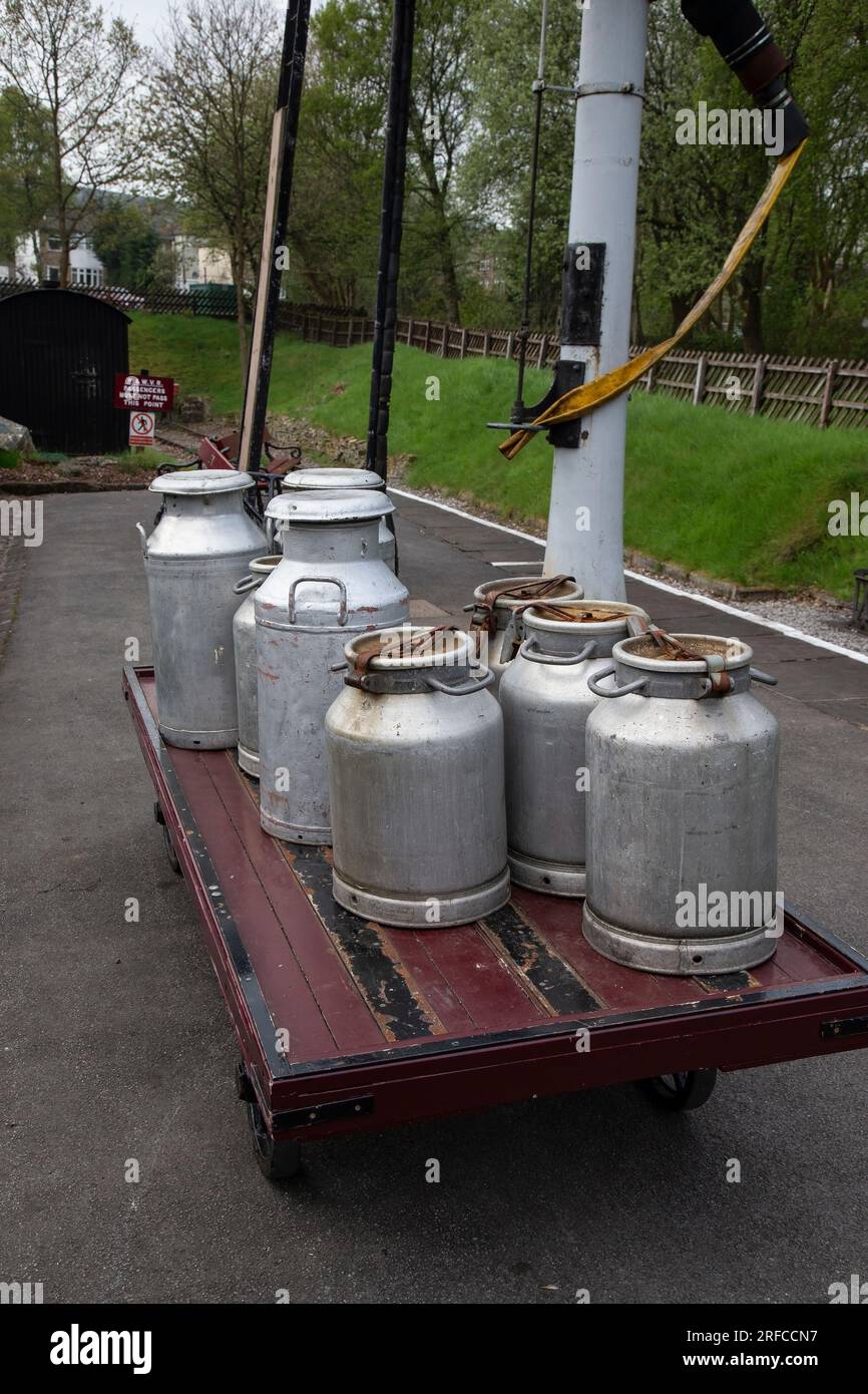 Traditionelle, authentische große konische und zylindrische Milchkannen auf einem hölzernen Bahnsteig-Trolley am Bahnhof Oxenhope der K&WV Railway Stockfoto