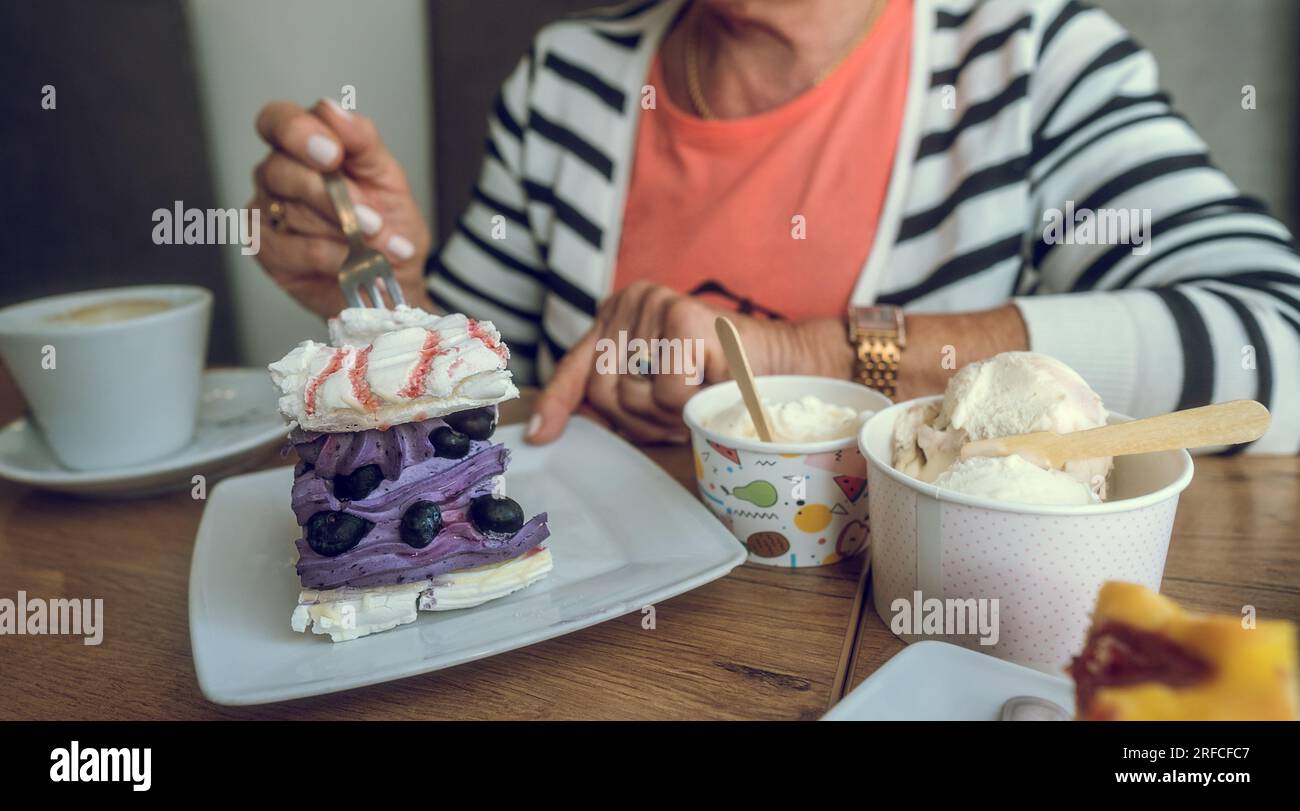 In einem Café. Lila Blaubeerkuchen, Eis und Kaffee auf dem Tisch. Hand einer älteren Frau mit Kuchengabel. Speicherplatz kopieren. Stockfoto