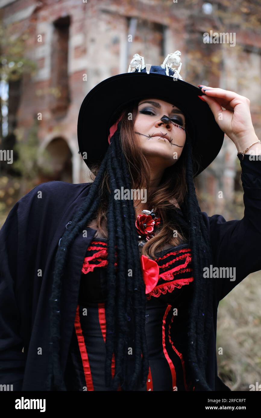 Eine Frau im Bild von Baron Saturday posiert vor dem Hintergrund eines alten Backsteingebäudes. Das Model trägt ein Korsett, eine Strickjacke und einen Hut Stockfoto