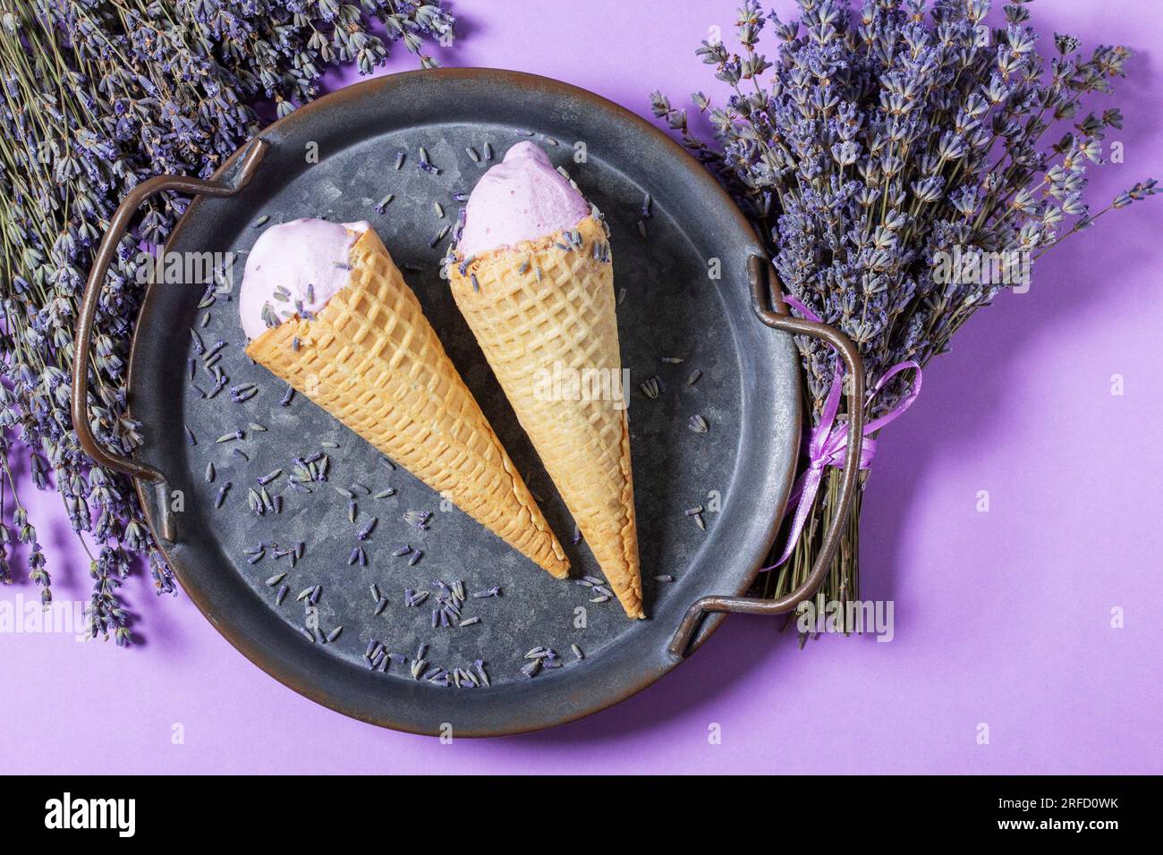 Zwei Lavendeleis in Waffle Cones auf einem Tablett und Blumensträuße aus trockenem Lavendel auf lila Hintergrund. Stockfoto