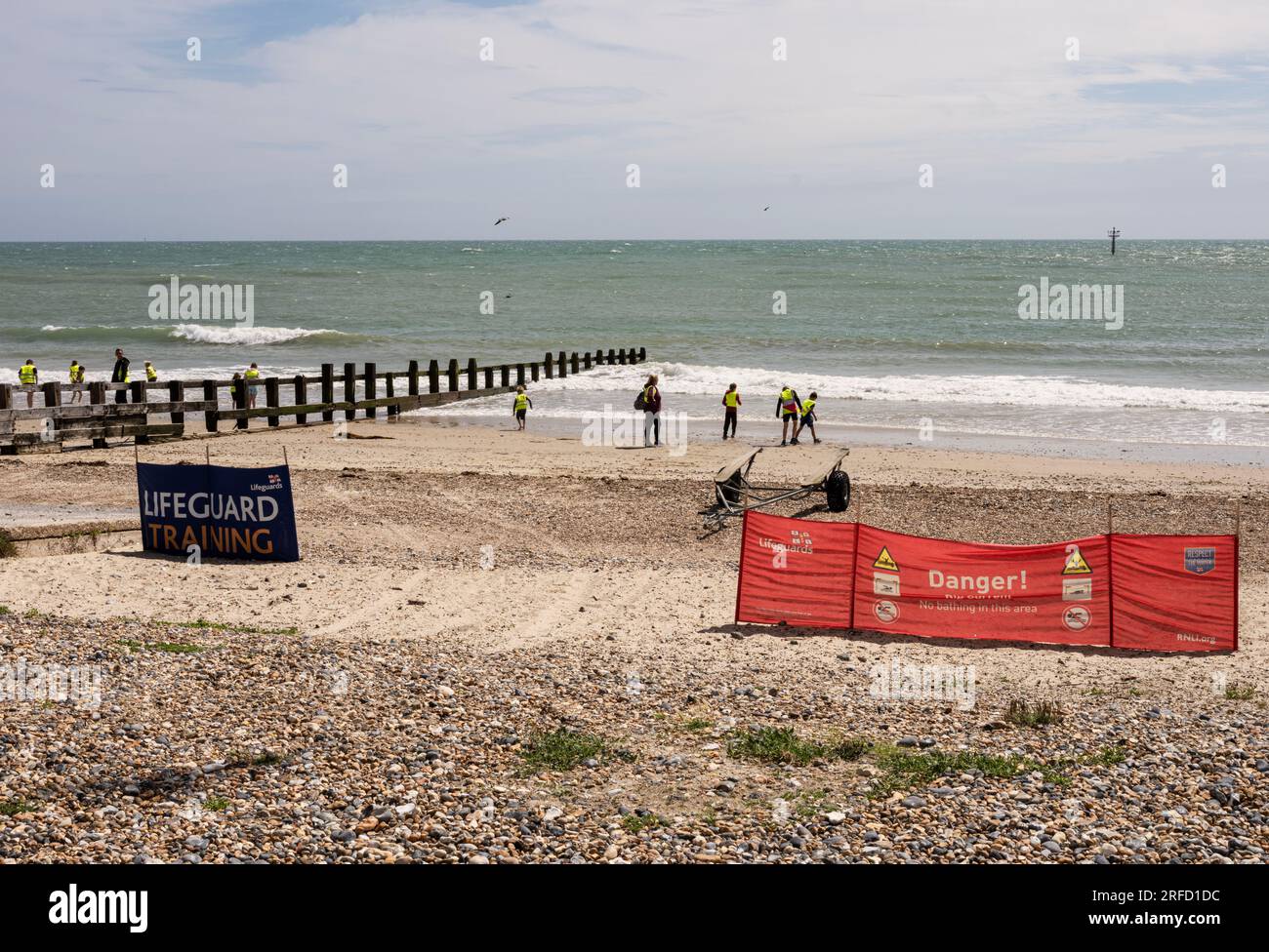 Promenade und Strand in Littlehampton, West Sussex, Großbritannien, im Sommer; Touristen am Strand in der Sonne, Windschutz und Rettungsschwimmer-Schild Stockfoto