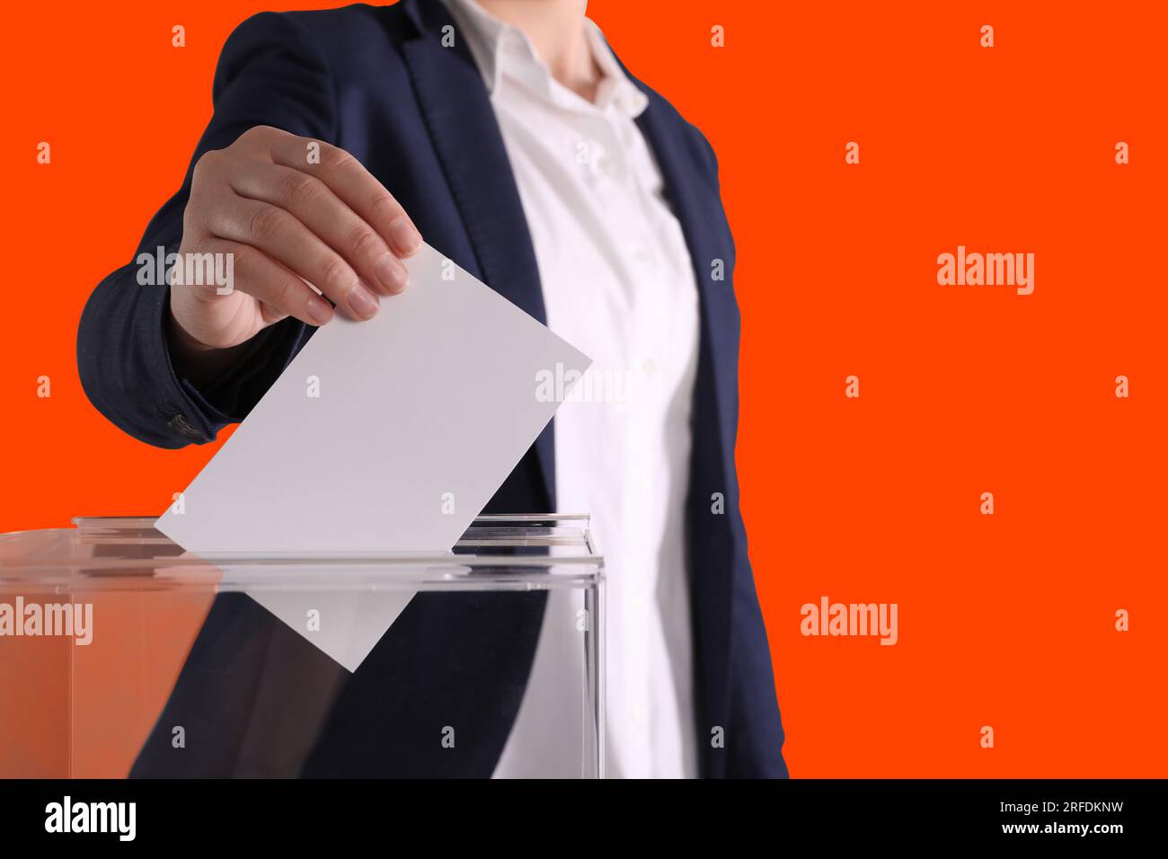 Eine Frau, die ihre Stimme in die Wahlurne auf dunkelorangefarbenem Hintergrund setzt, Schließung Stockfoto