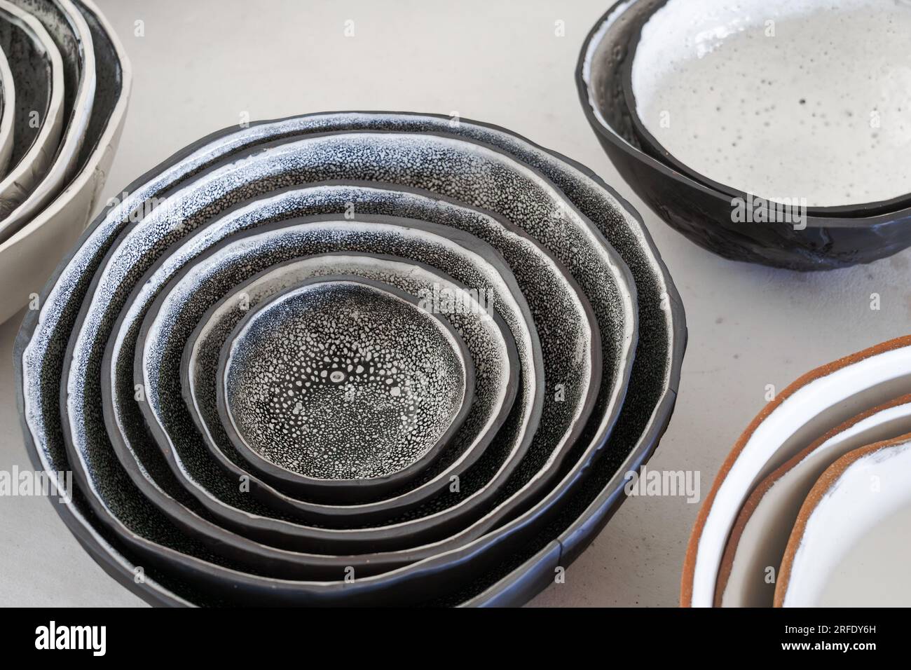 Eine Sammlung verschiedener handgemachter Tonschüsseln mit schwarz-weiß gesprenkelter Glasur und Terrakotta auf einem Tisch. Stockfoto