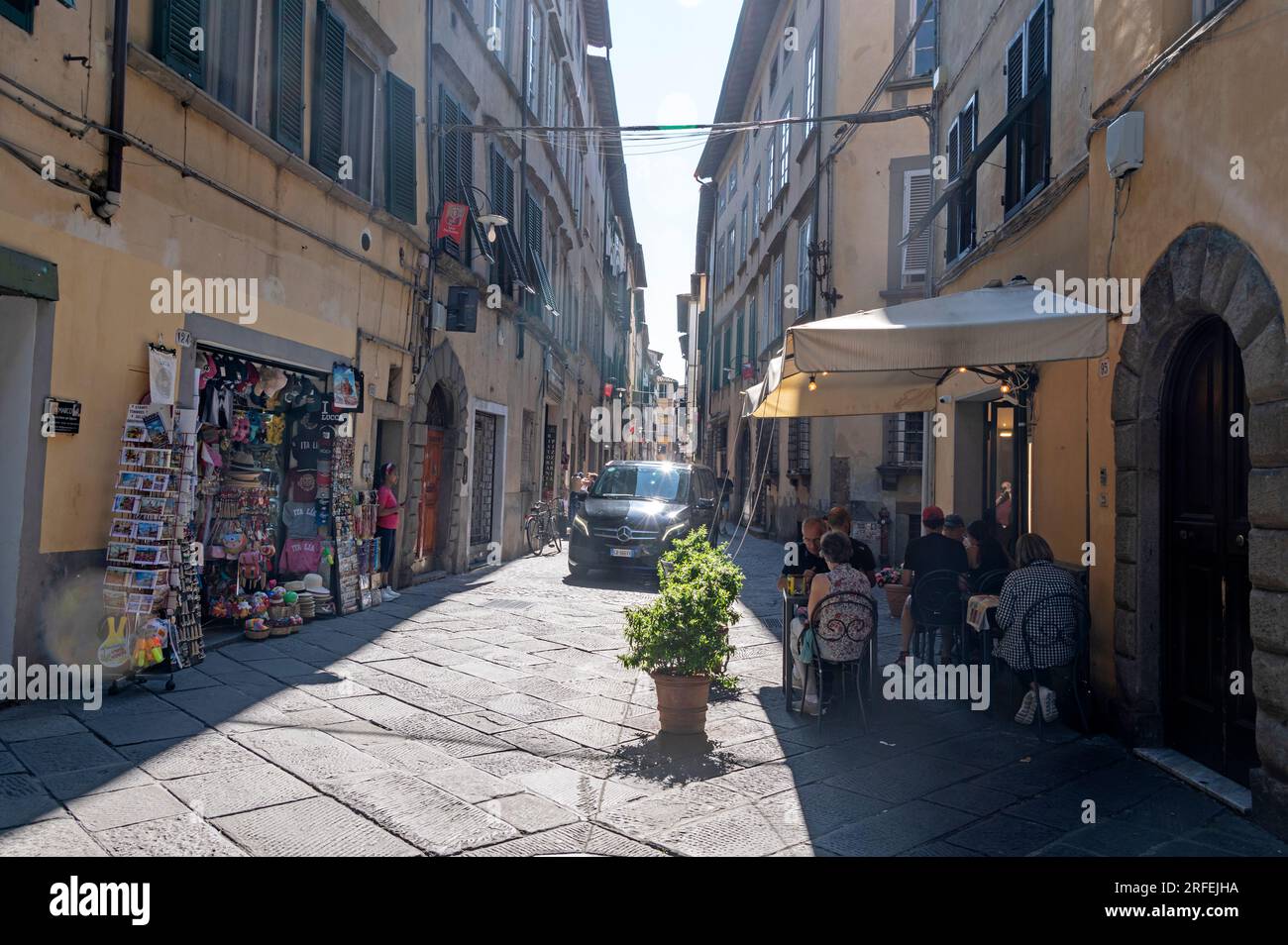 Ein Auto, das durch eine mittelalterliche, enge Kopfsteinpflasterstraße fährt, die in der Regel von Touristen in der Stadt Lucca in der Toskana Italiens gefüllt ist. Stockfoto