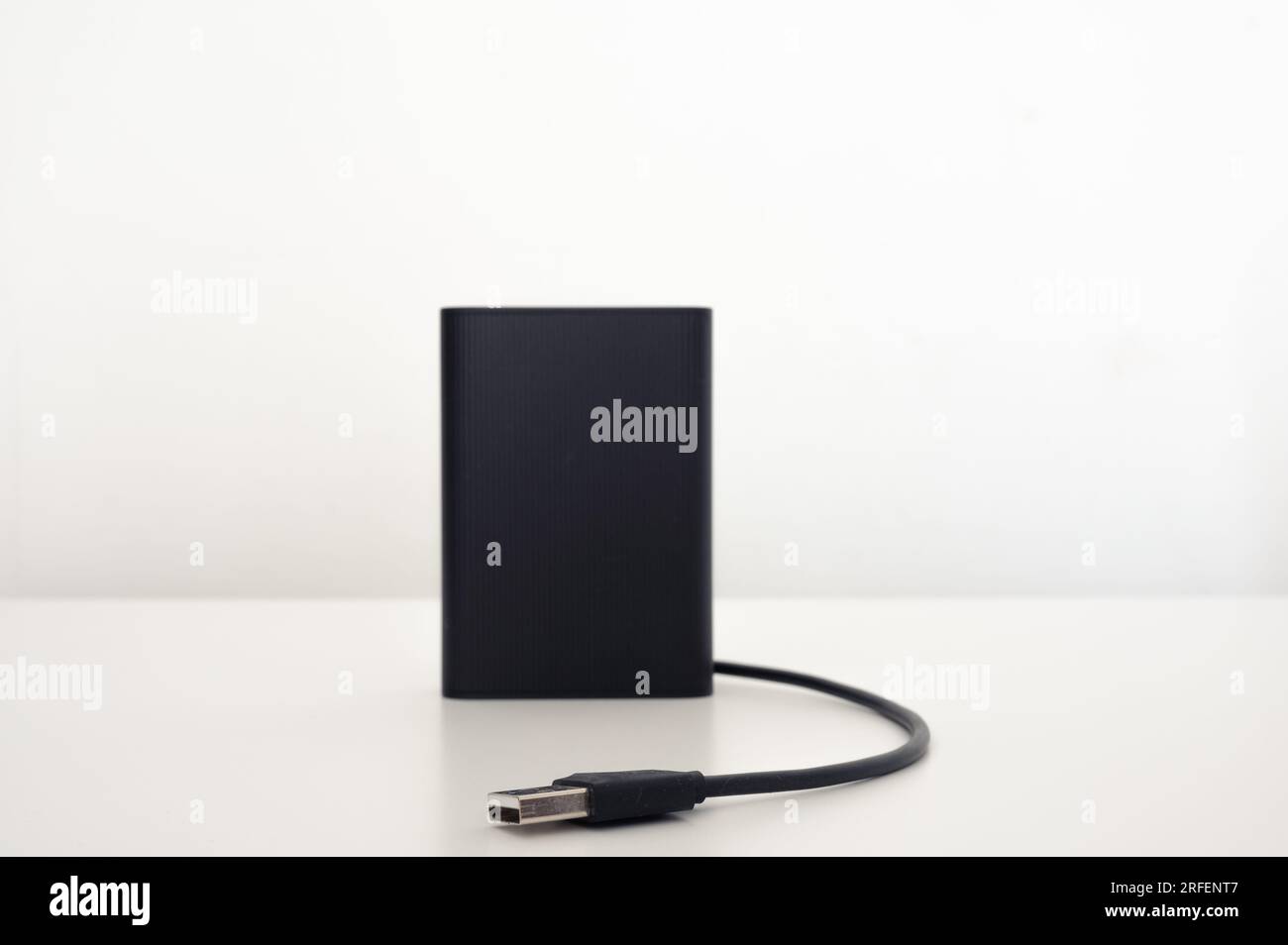 Schwarzes mobiles Ladegerät auf dem Tisch mit einem schwarzen isolierten usb-Kabel. Weißer Hintergrund. Stockfoto