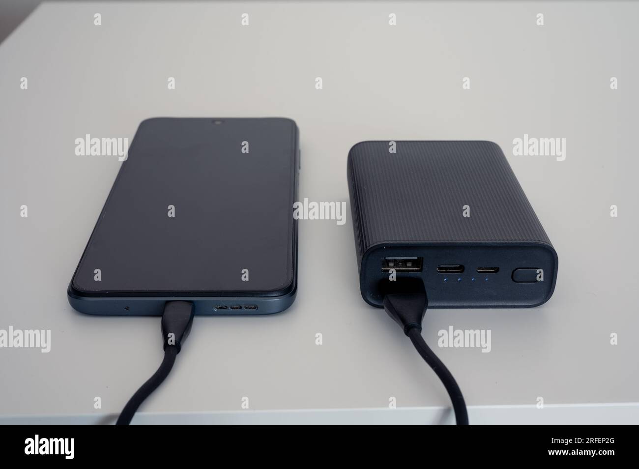 Schwarze Powerbank zum Aufladen des Mobilgeräts. Schwarzes Kabel. Auf weißem Hintergrund Stockfoto