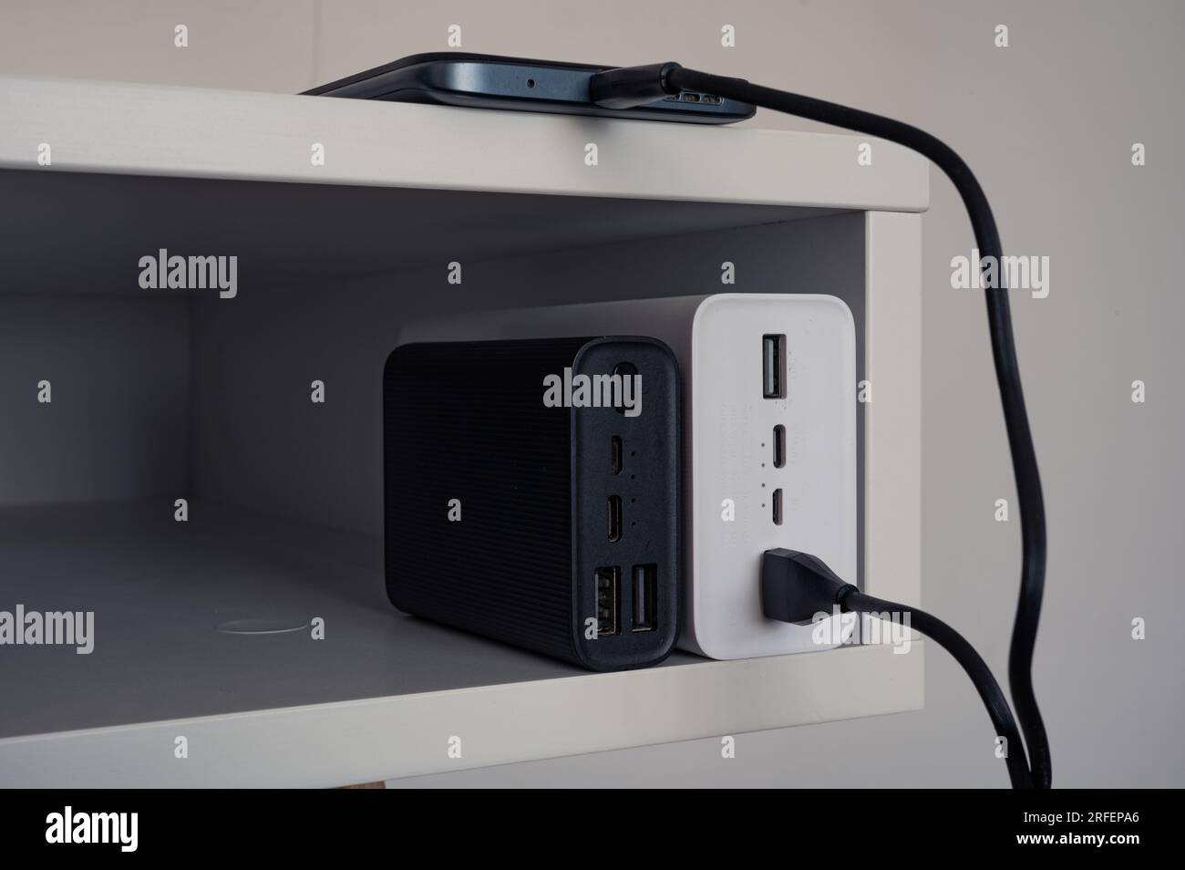 Aufladen des Smartphones mit der weißen Powerbank. In der Nähe steht die schwarze Powerbank. Stockfoto