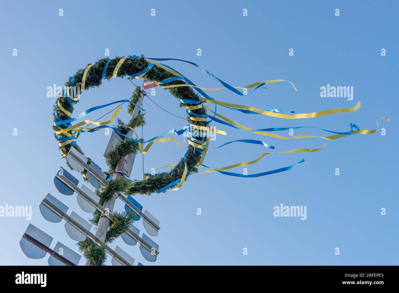 Maypole mit Kranz, Bändern und Wappen vor blauem Himmel Stockfoto