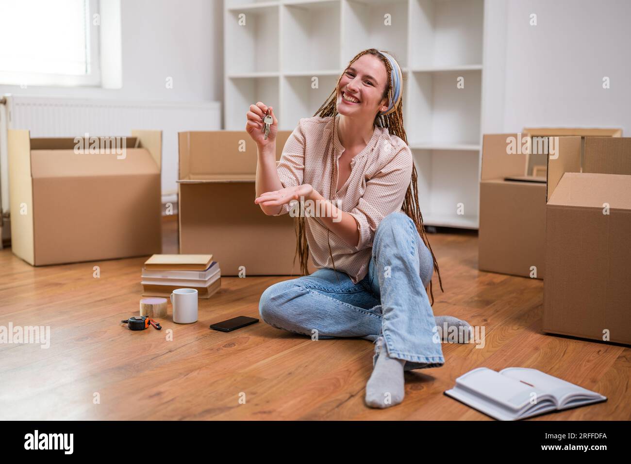 Moderne Ingwerfrau mit Zöpfen, die den Schlüssel zu ihrem neuen Zuhause zeigen. Stockfoto