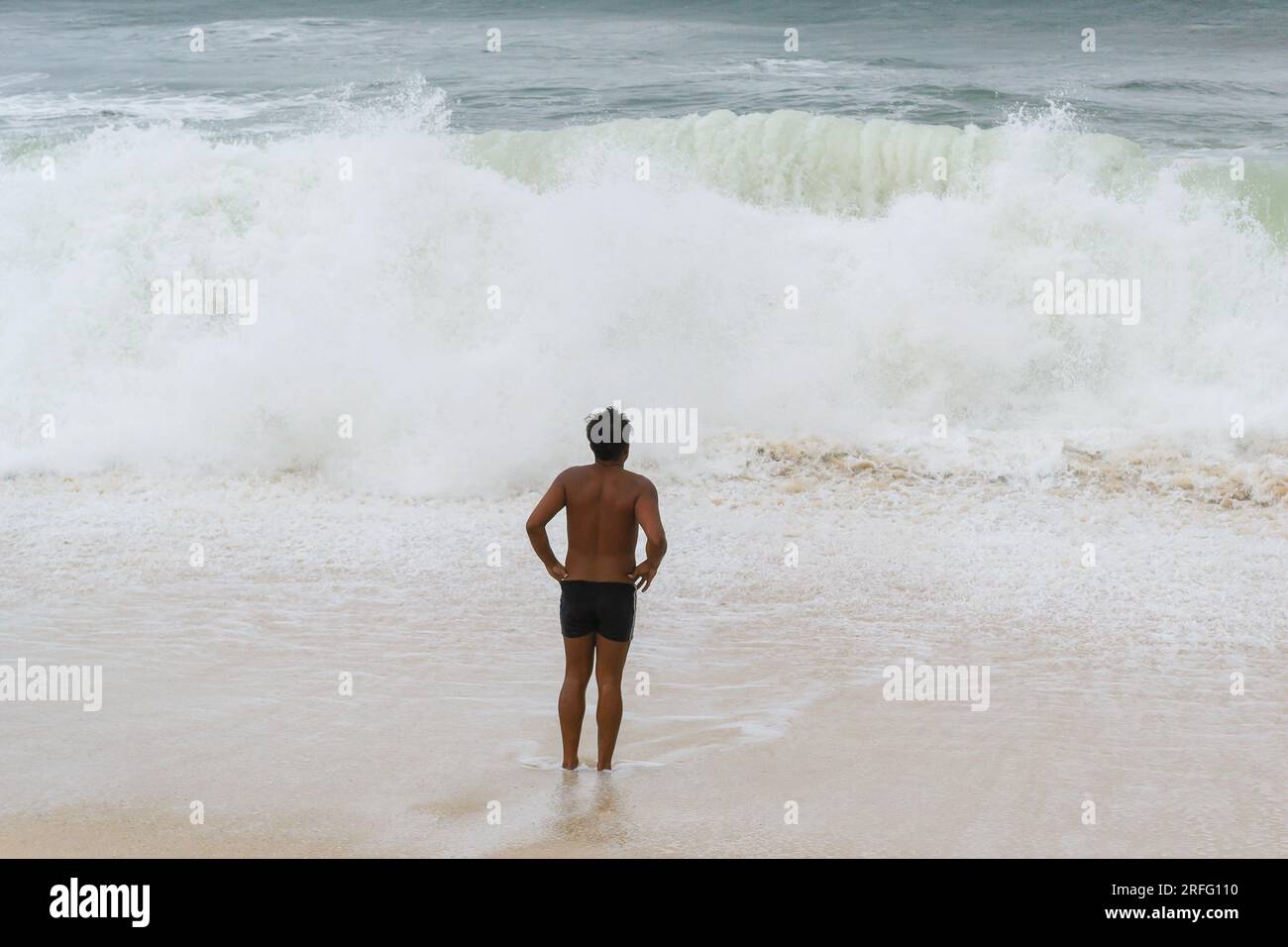Niteroi, Brasilien, Ein junger brasilianischer Mann beobachtet gewaltige Wellen, die am Strand brechen Stockfoto