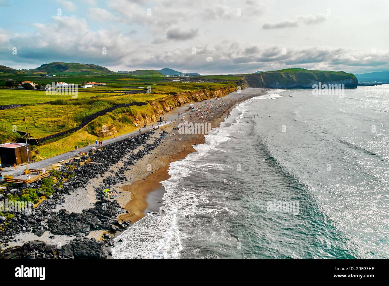 Blick aus der Vogelperspektive auf die felsige Küste und den Sandstrand mit Touristen, die sich an der Küste in der Nähe des Atlantischen Ozeans entspannen, wolkiger Himmel. Sao Miguel Island, Azoren, Portugiesisch Stockfoto