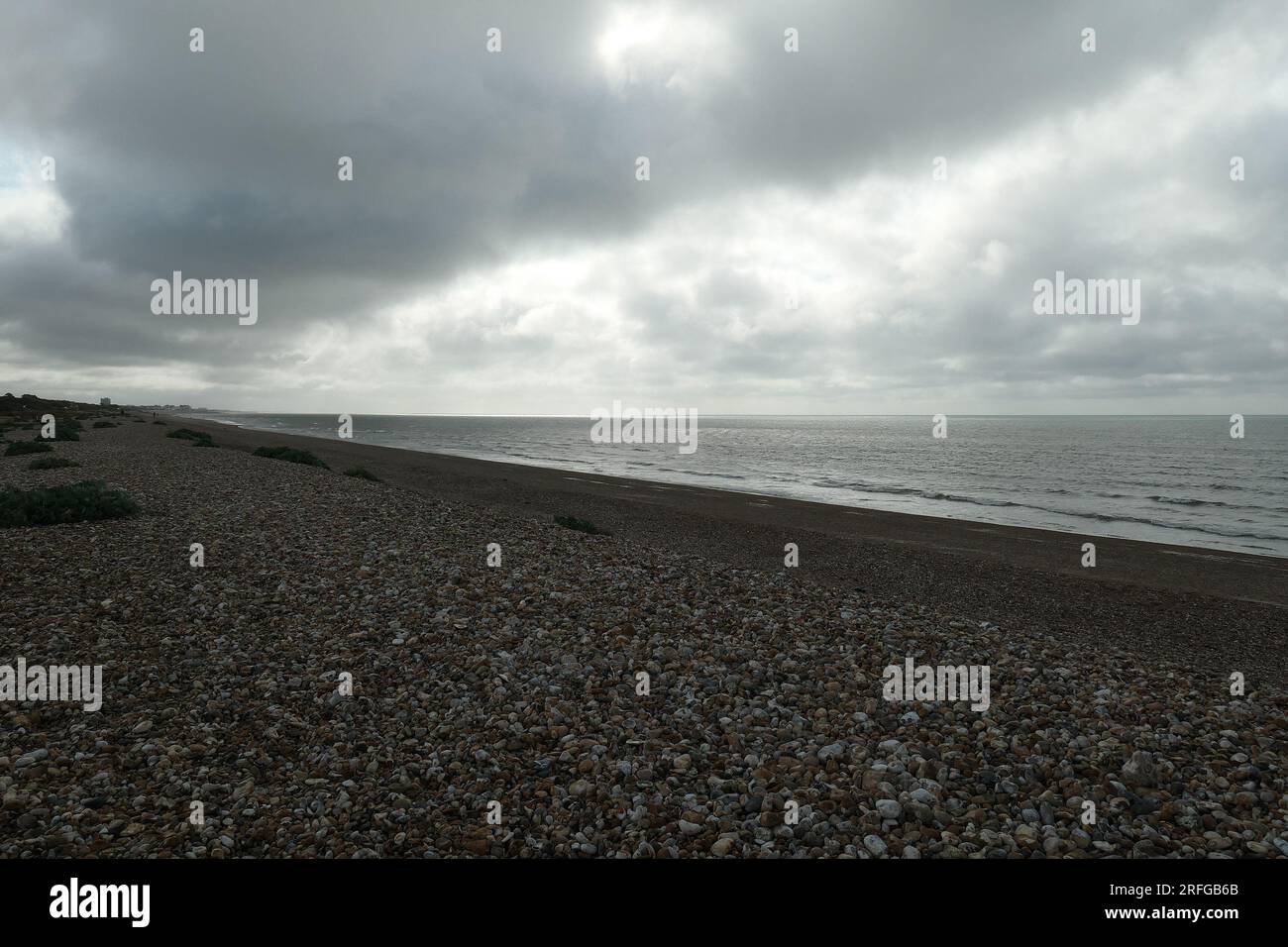 Dunkle Wolkenbänke über dem Kieselstrand und dem Meer an der Südküste Großbritanniens. Stockfoto