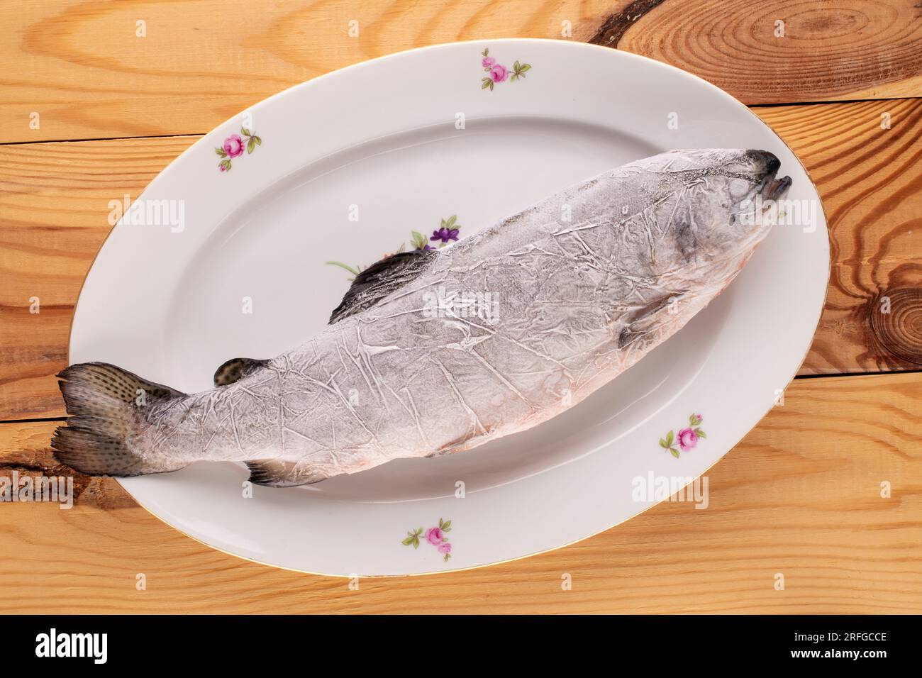 Eine gefrorene Forelle mit weißer Keramikplatte auf einem Holztisch, Makro, Draufsicht. Stockfoto