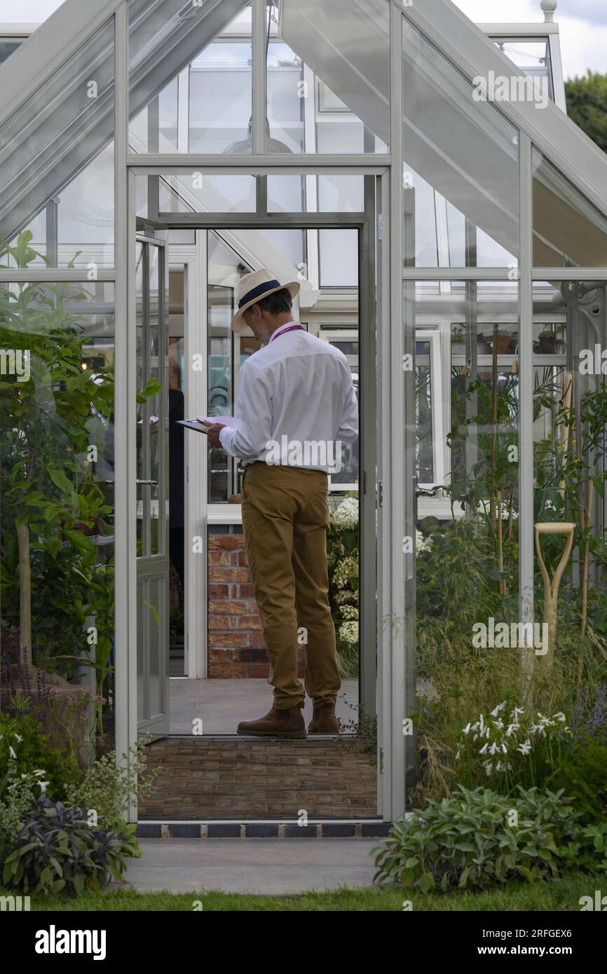 Vertriebsmitarbeiter steht neben Werken im ausgestellten Gewächshaus, Hartley Botanic „Feel Good“-Messestand – RHS Tatton Park Flower Show, 2023, Cheshire England, Großbritannien. Stockfoto
