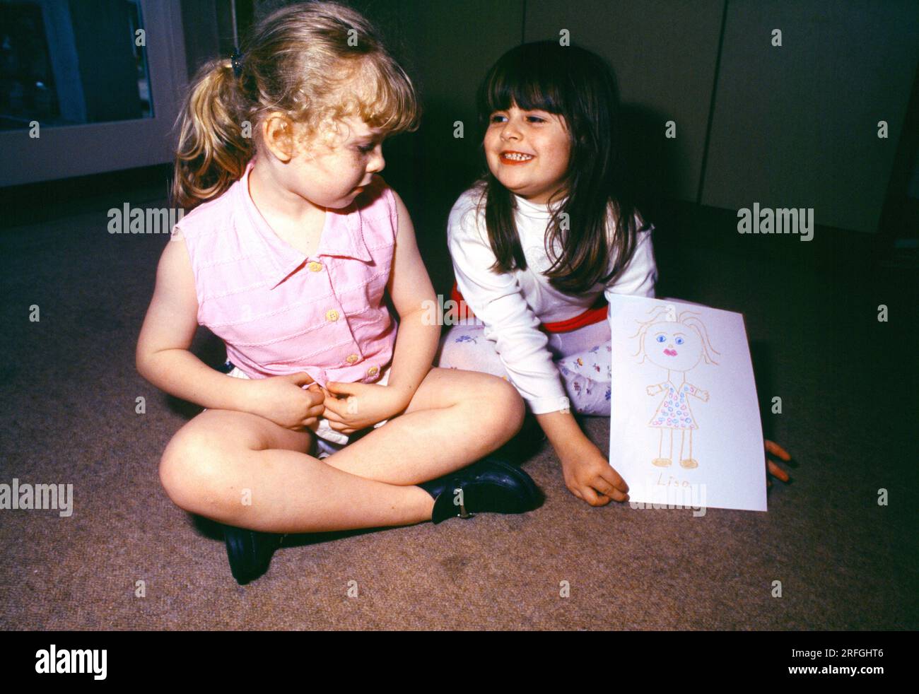 Zwei sprechende Mädchen sitzen quer auf dem ersten Stock und zeichnen von ihrem Freund England Stockfoto