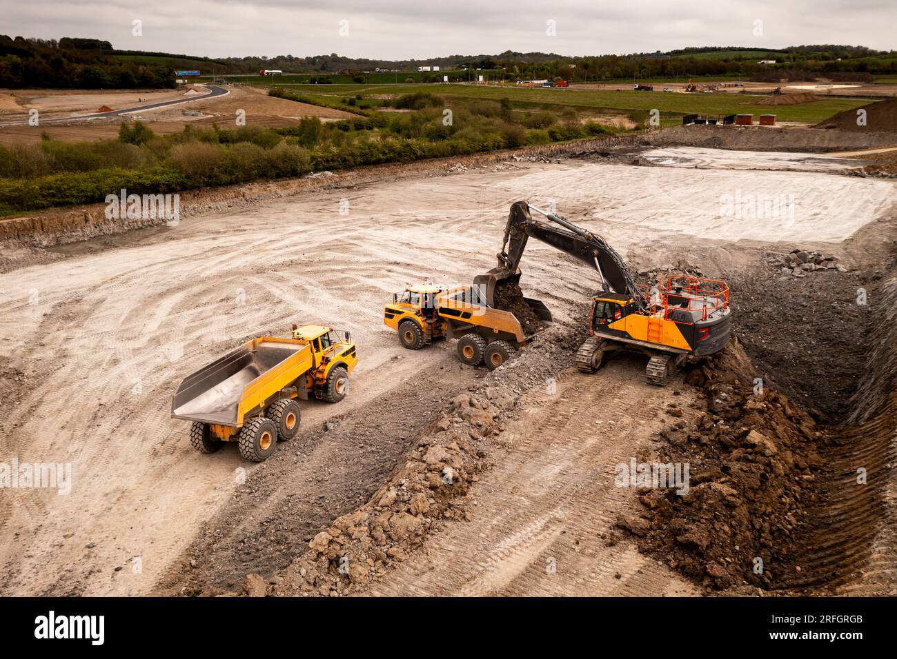 Luftaufnahme direkt über einem Kran oder einem mechanischen Bagger mit Greiferbeladung eines Muldenkippers mit Erde und Erde in der Bauindustrie auf einem Brownfi Stockfoto