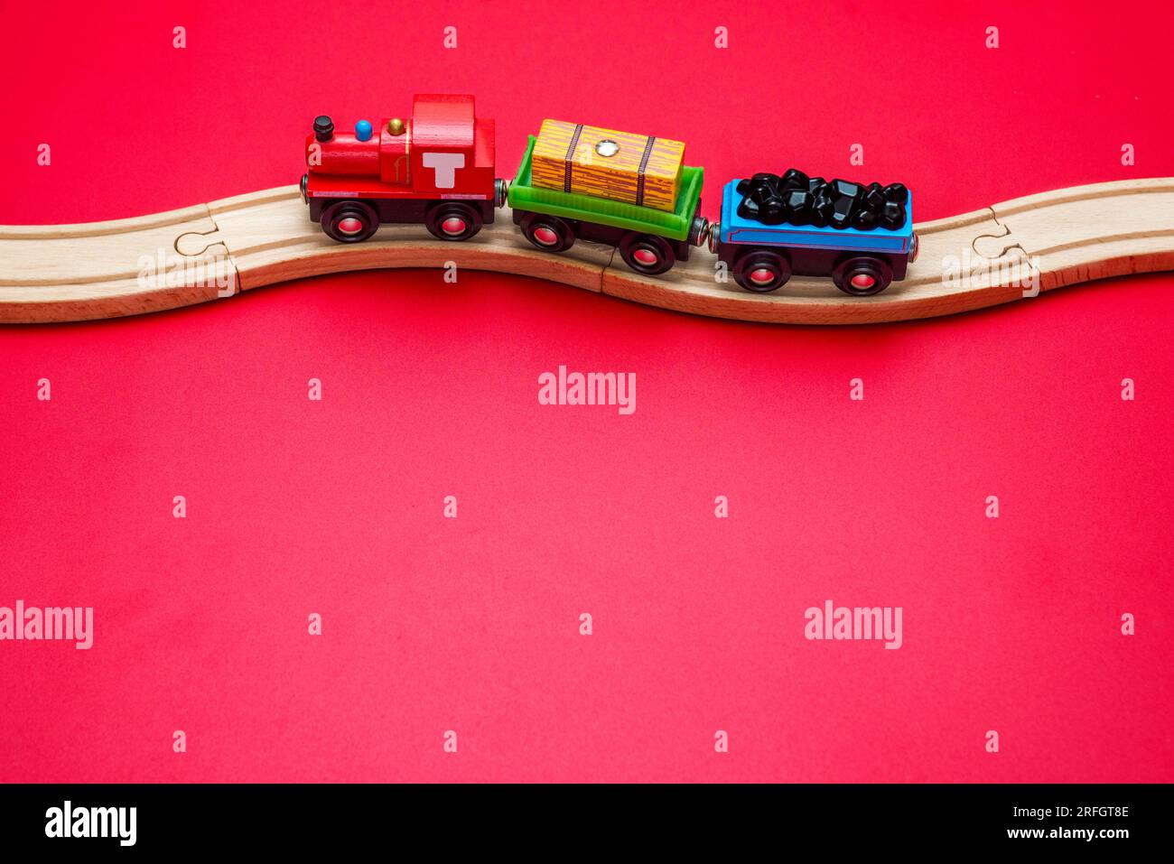 Spielzeugzug mit gebogenen Holzschienen auf rotem Hintergrund. Holzlokomotive. Stockfoto