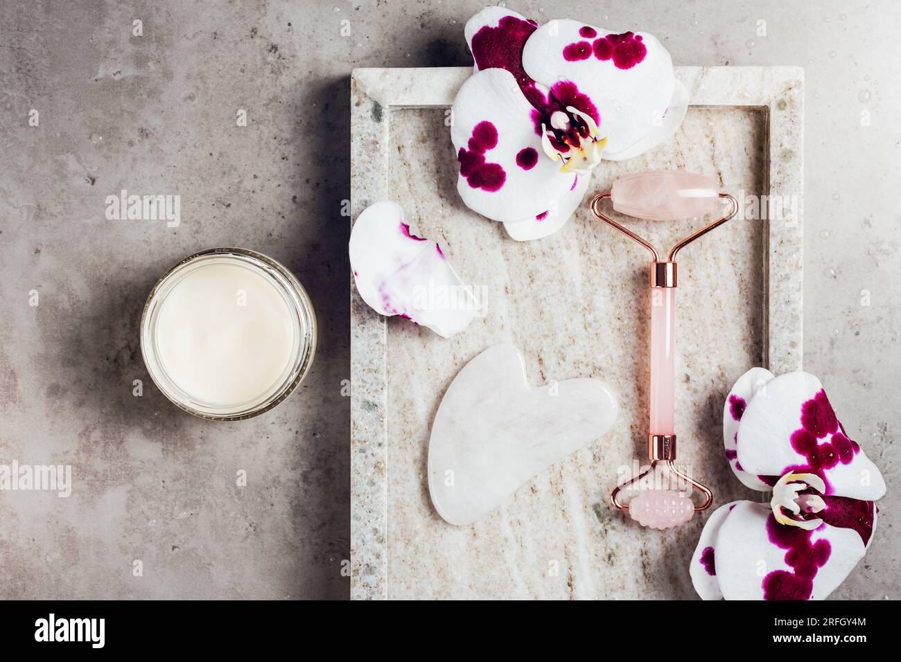 Rosa Quarzwalze, Gua Sha und Orchideenblumen auf Marmorhintergrund. Spa-Konzept, Gesichtspflege. Stockfoto