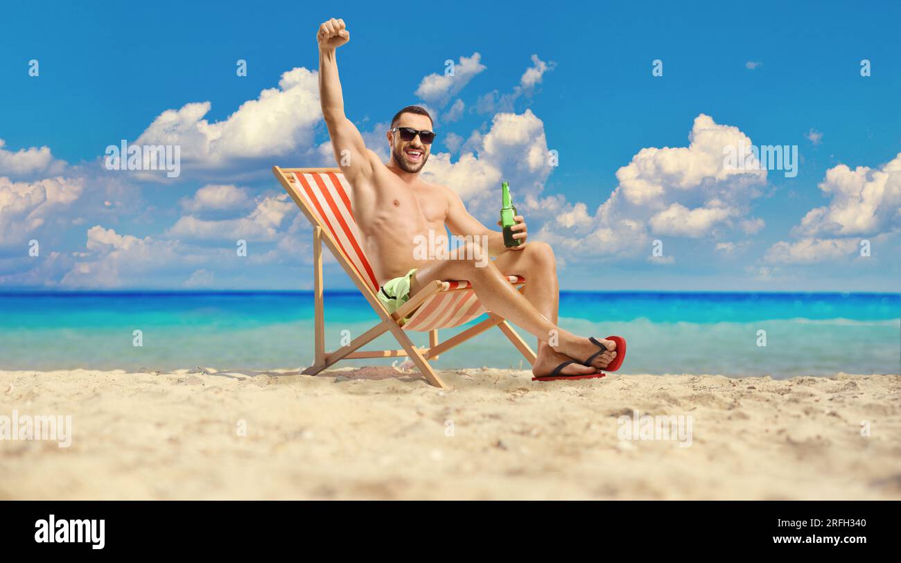 Ein Mann am Strand am Meer, der eine Flasche Bier in der Hand hält und Glück bringt Stockfoto