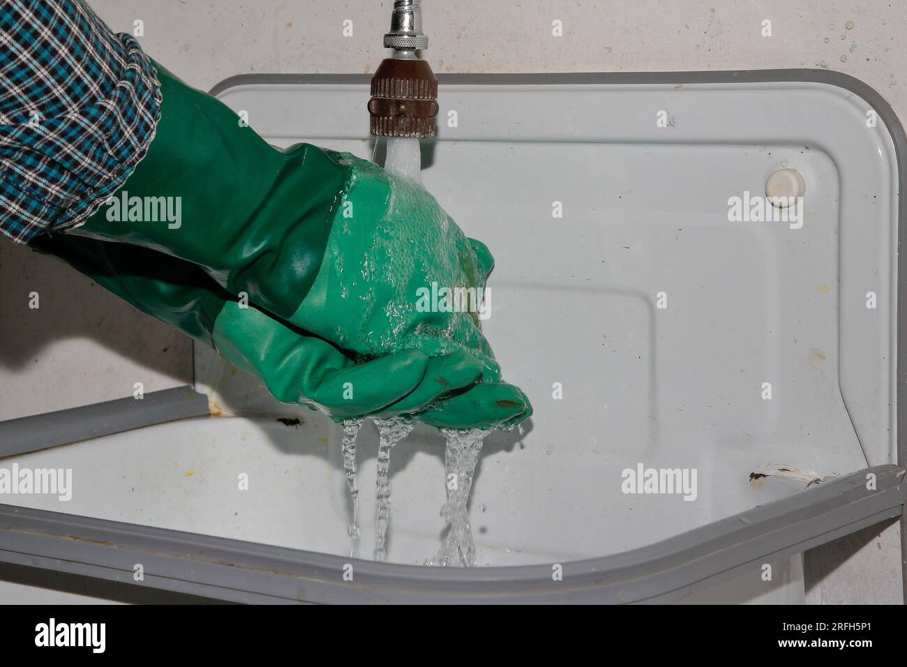 Ein Mann legt seine Hände mit grünen Gummihandschuhen unter fließendes Wasser. Hüten Sie sich vor dem Grünwaschen! Stockfoto