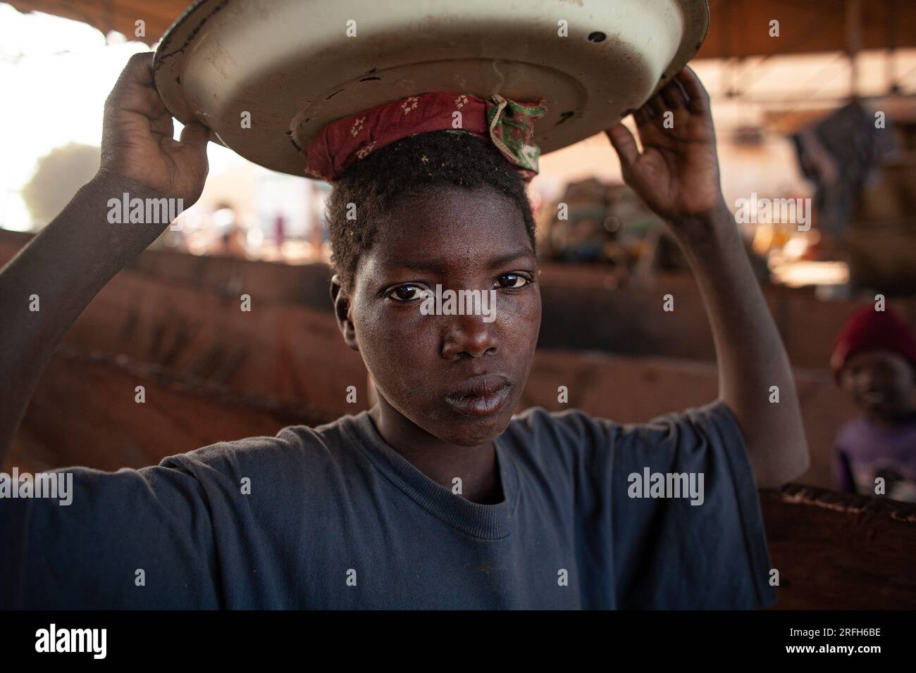 Westafrikanischer Junge, kehrt ins Dorf zurück, trägt Essen auf dem Kopf. Nahrungsmittelversorgung in ländlichen Gemeinden. Mali, Westafrika. Stockfoto