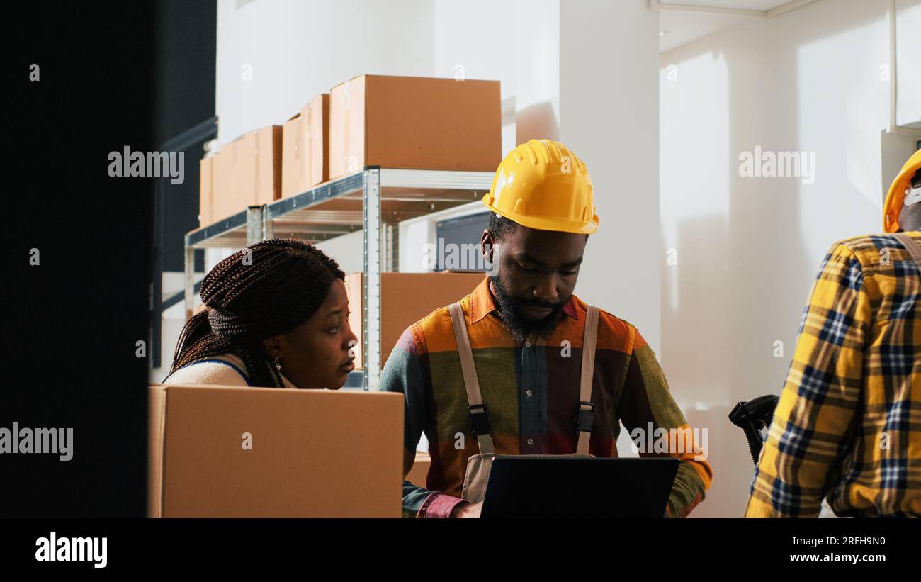 afroamerikanische Menschen, die Zubehör planen, bestellen mit einem Laptop im Lagerraum und prüfen vor der Herstellung von Waren Kartons mit Einzelhandelsprodukten. Mitarbeiter, die an der Qualitätskontrolle arbeiten. Stockfoto