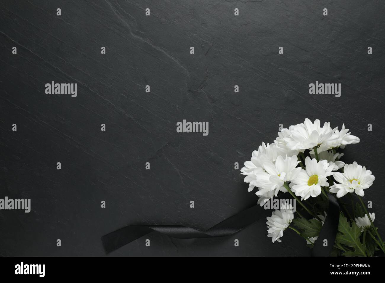 Weiße Chrysanthemen und Band auf schwarzem Tisch, Draufsicht mit Platz für Text. Begräbnissymbole Stockfoto