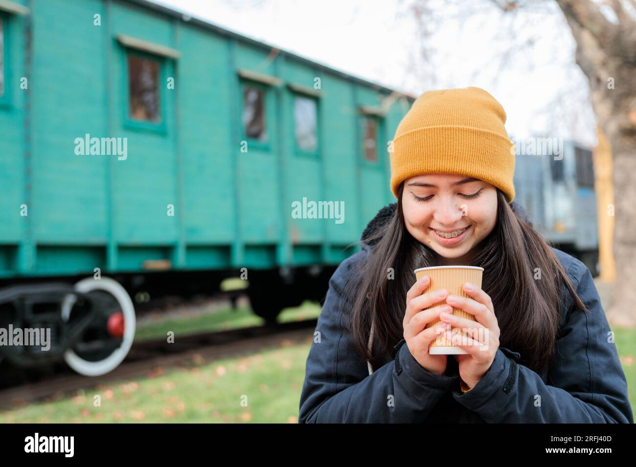 Kaffeepause im Bahnhofsgebäude: Junge Latina in warmer Kleidung, die eine Tasse Kaffee zum Mitnehmen isst. Speicherplatz kopieren Stockfoto