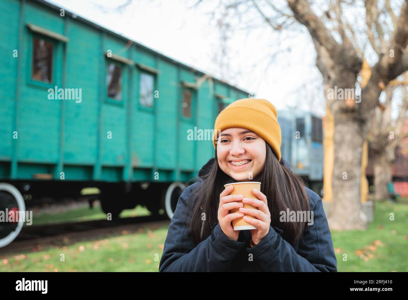 Gemütliche Vibes: Latina Girl, gekleidet in Winterkleidung, verwöhnt sich mit einem Kaffee zum Mitnehmen im Railway Park Stockfoto