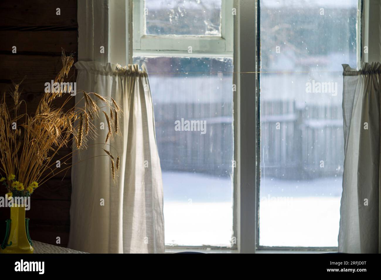 Altes Holzhaus mit Roggenstrauß neben dem Fenster, Winterlandschaft draußen Stockfoto