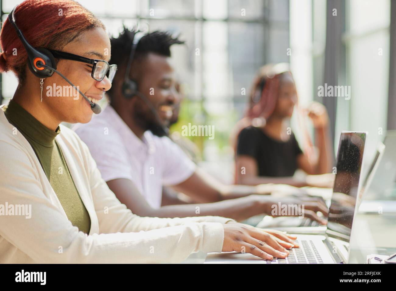 Junge Callcenter-Mitarbeiter sitzen an einem Laptop und helfen bei der Lösung von Problemen Stockfoto