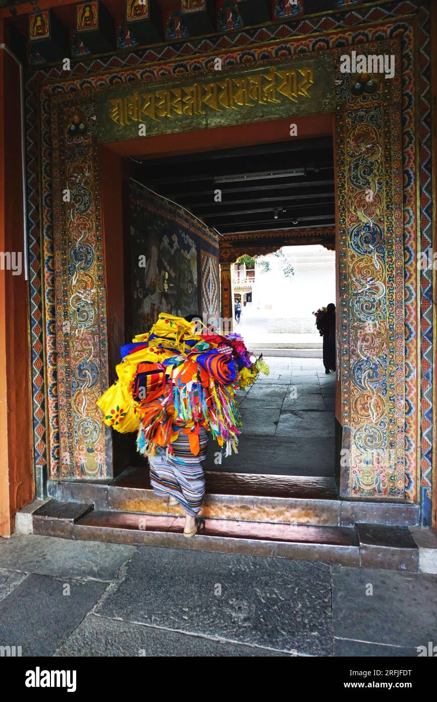 Versteckt unter einem Bündel farbenfroher Tempelbanner aus Stoff betritt ein Arbeiter die kunstvoll geschnitzte, bemalte Tür von Punakha Dzong im Königreich Bhutan Stockfoto