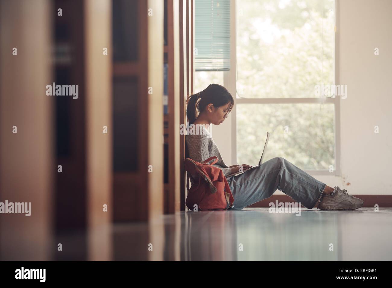 Studentin, die auf dem Boden sitzt und einen Laptop benutzt, schreibt Notizen für Papier, Essay, Lernen für Klassenaufgabe. Vielfältige Gruppe von Schülern lernen, studieren Stockfoto