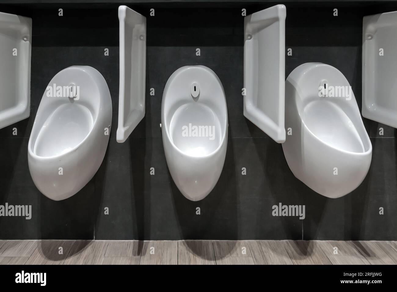 Drei weiße Urinale in der öffentlichen schwarzen Toilette Stockfoto