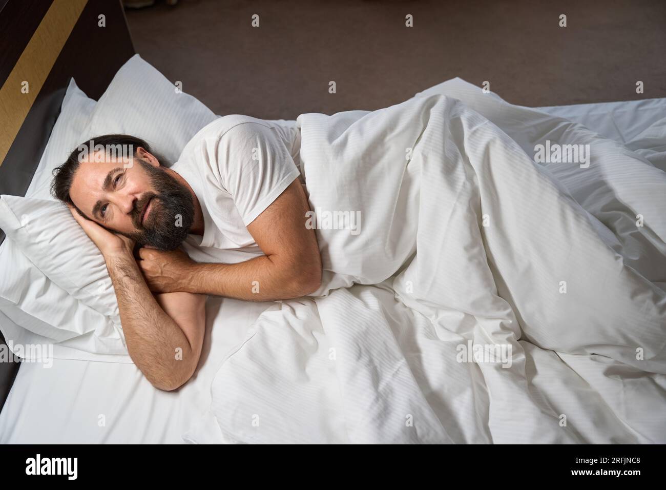 Erwachter Mann sonnt sich in einem großen Bett, er ist Gast eines komfortablen Hotels Stockfoto