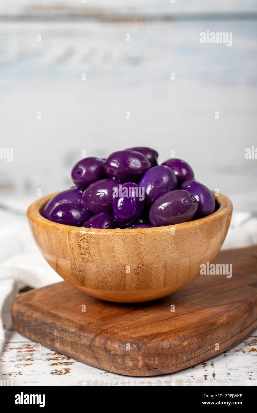 Fermentierte Oliven mit Heidelbeeren in einer Holzschüssel. Lila Oliven auf weißem Holzhintergrund. Mediterrane Küche. Veganes Essen Stockfoto