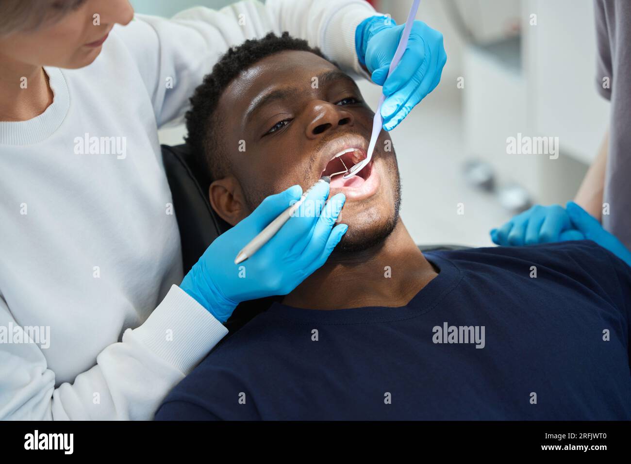 Konzentrierte Frau Zahnärztin prüft Gesundheit von afroamerikanischen Klienten Zähnen mit Mundspiegel und Sichelsonde, jeden Zahn berühren, um Schmelz q zu prüfen Stockfoto