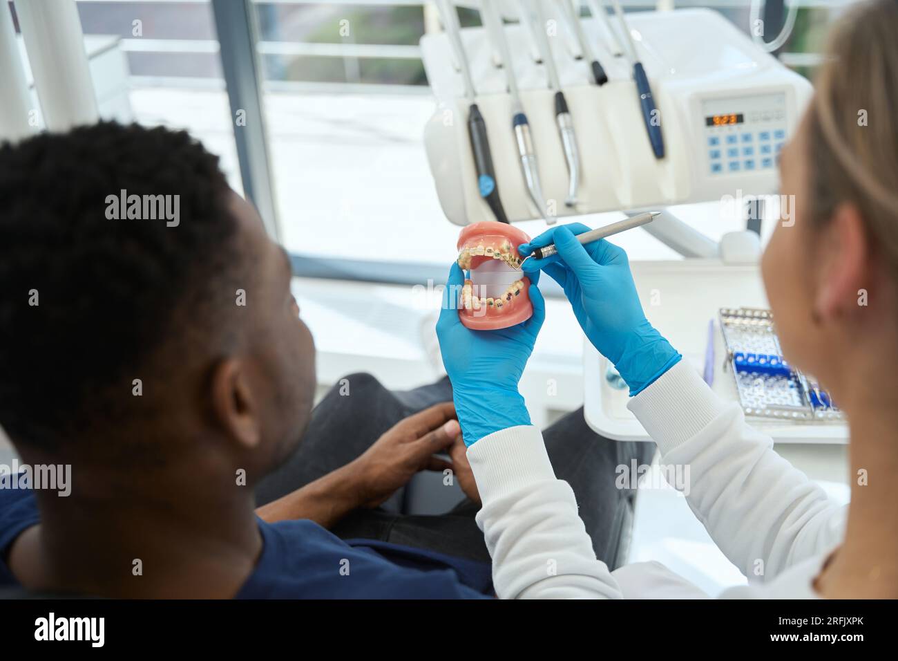 Zahnarzt mit Sichelsonde, um dem männlichen Klienten seine Probleme am Kiefermodell zu zeigen, Arzt und Patient diskutieren Prothetik, ästhetische Stomatologie Stockfoto