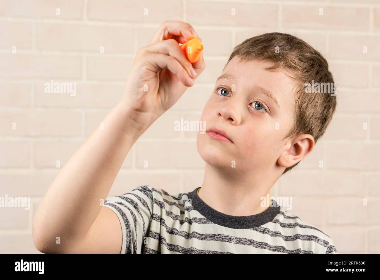 Ein glücklicher weißer Junge im Schulalter schreibt in der Luft mit einem orangefarbenen Marker. Das Konzept von Studium, Schultätigkeit und Bildung Stockfoto