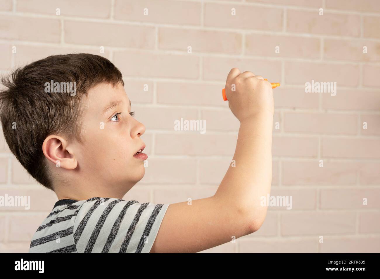 Ein glücklicher weißer Junge im Schulalter schreibt in der Luft mit einem orangefarbenen Marker. Das Konzept von Studium, Schultätigkeit und Bildung Stockfoto