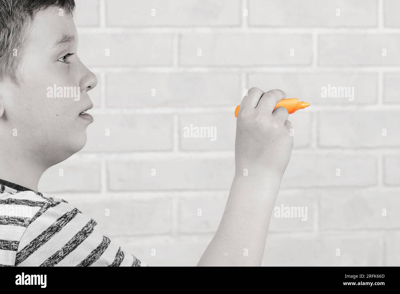 Ein glücklicher weißer Junge im Schulalter schreibt in der Luft mit einem orangefarbenen Marker. Das Konzept von Studium, Schultätigkeit und Bildung Stockfoto