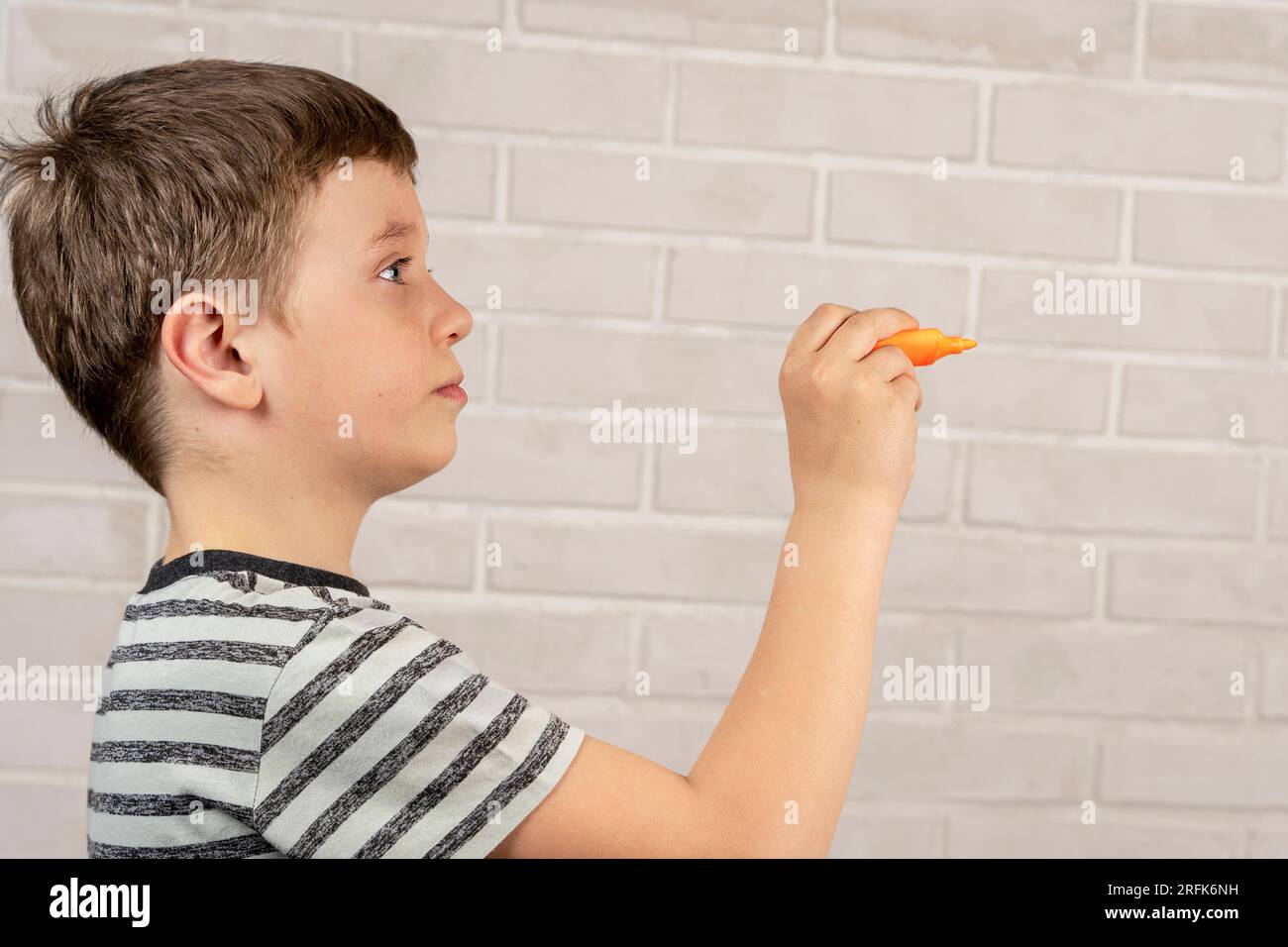 Ein glücklicher weißer Junge im Schulalter schreibt in der Luft mit einem orangefarbenen Marker. Das Konzept von Studium, Schultätigkeit und Bildung Stockfoto