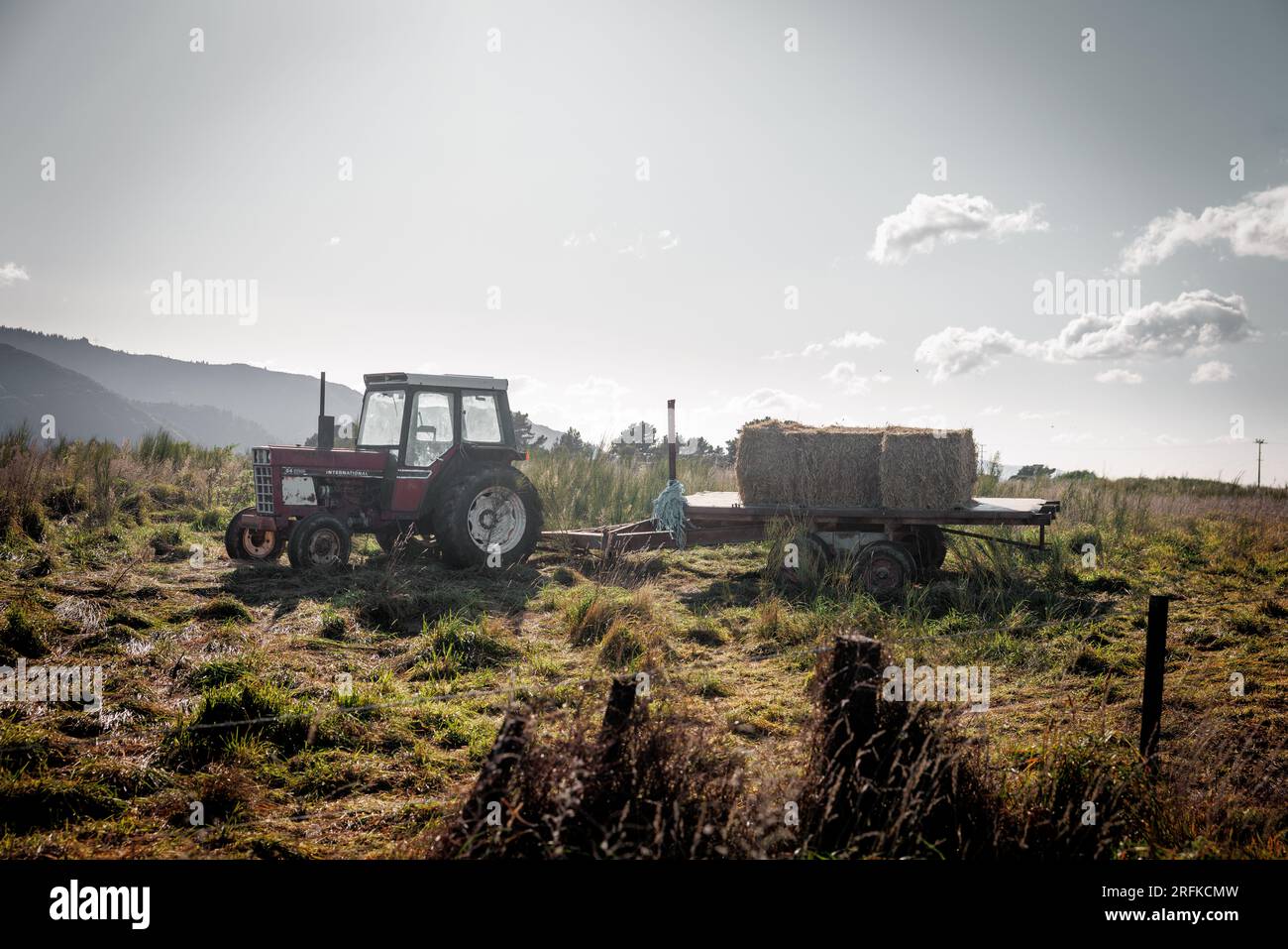 Ein Bild eines alten Traktors, der auf einem Feld mit der Sonne dahinter sitzt. Stockfoto