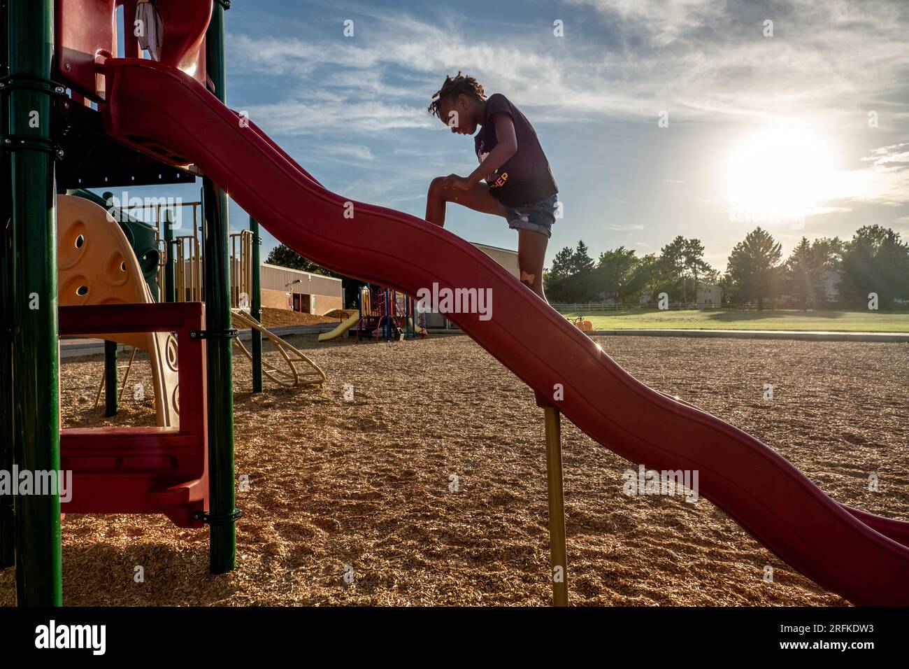 Ein afroamerikanisches Mädchen klettert eine Rutsche in einem Park hoch Stockfoto