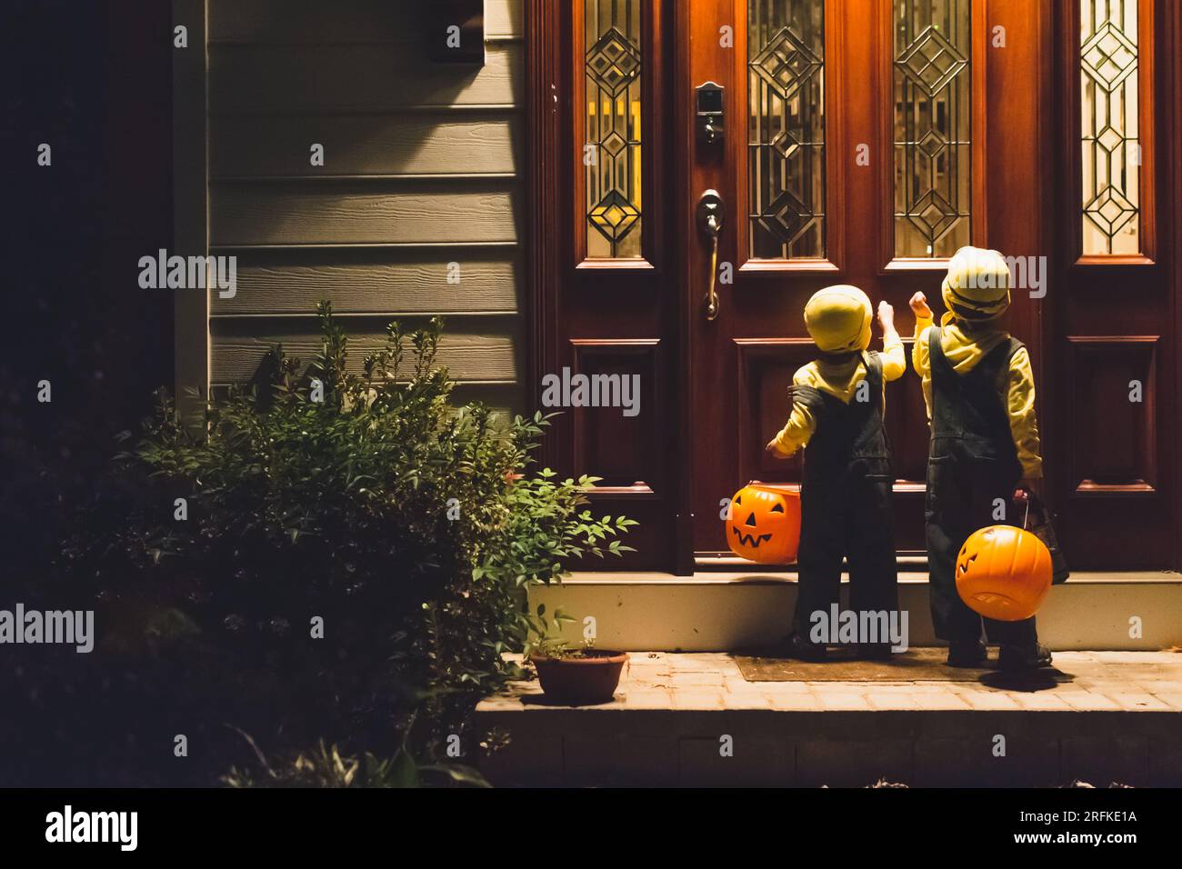 Junge Jungen klopfen an die Haustür, um an Halloween zu tricksen oder zu verwöhnen. Stockfoto