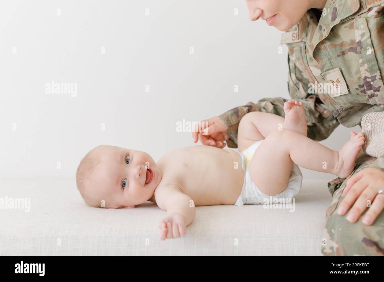 Aktive militärmutter, die mit dem Baby spielt, während sie seine Windel wechselt Stockfoto