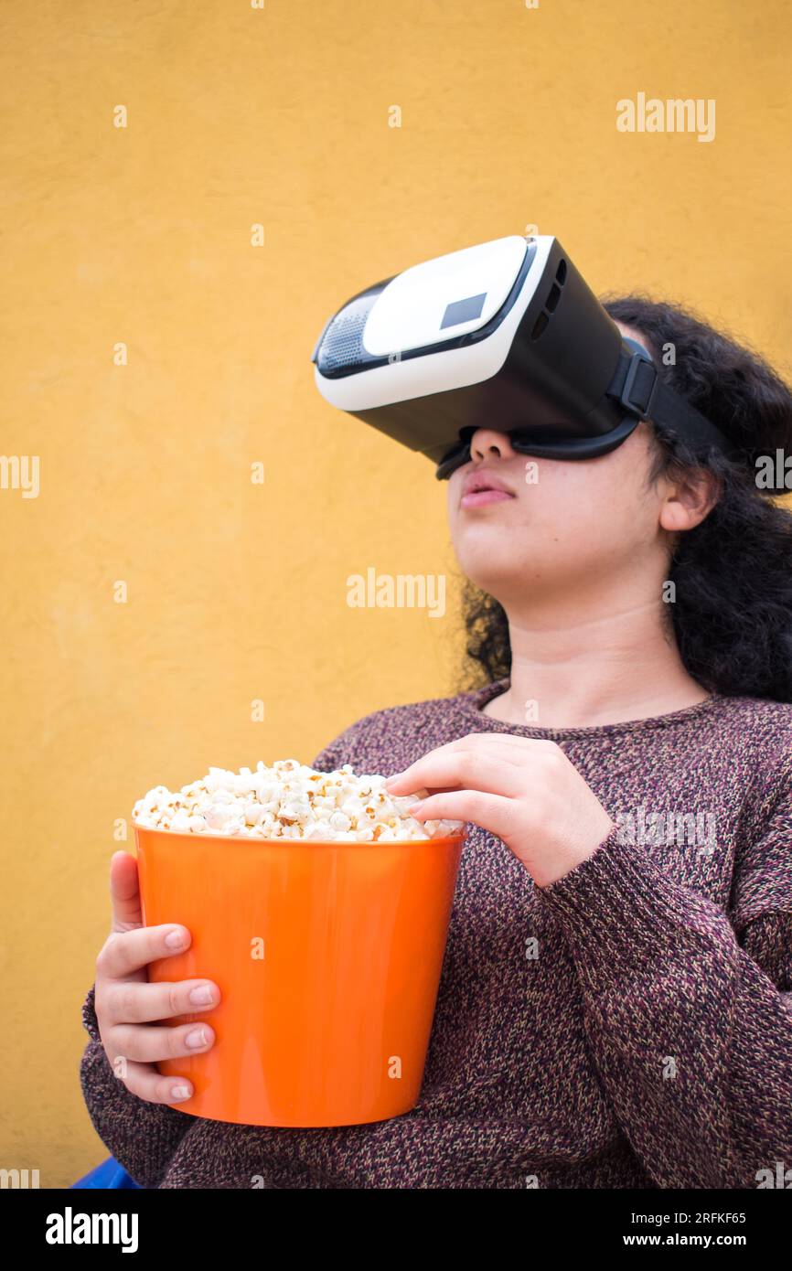 Eine Frau trägt ein Headset und isst Popcorn aus dem Orangentopf Stockfoto