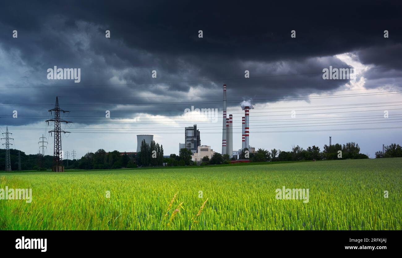Dunkle Wolken über einem Kohlekraftwerk unter einem grünen Weizenfeld Stockfoto