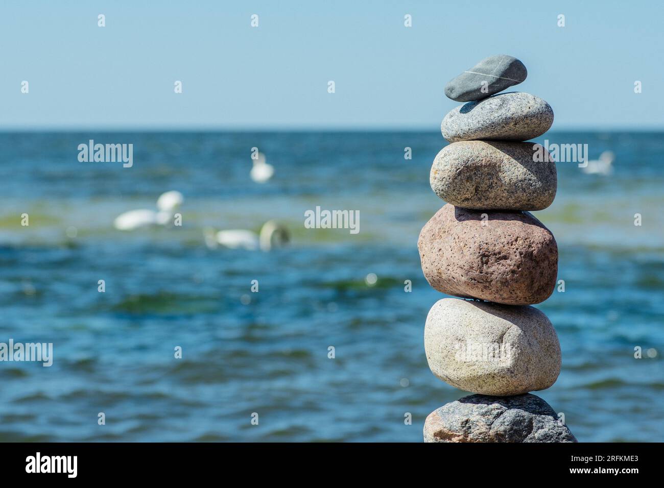 Balancieren von Steinen auf einem großen Felsen mit Seegras am Strand, mit blauen Wasserwellen im Hintergrund, Ostsee, Olando Kepure, Litauen Stockfoto