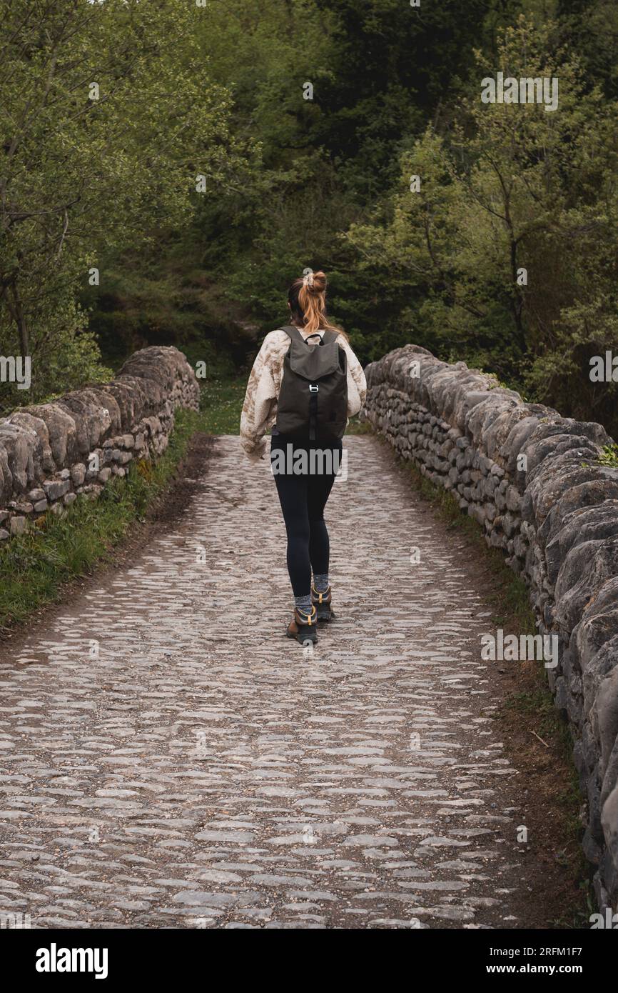 Junge Frau mit Rucksackwandern und Überquerung einer alten Steinbrücke mitten im Wald Stockfoto